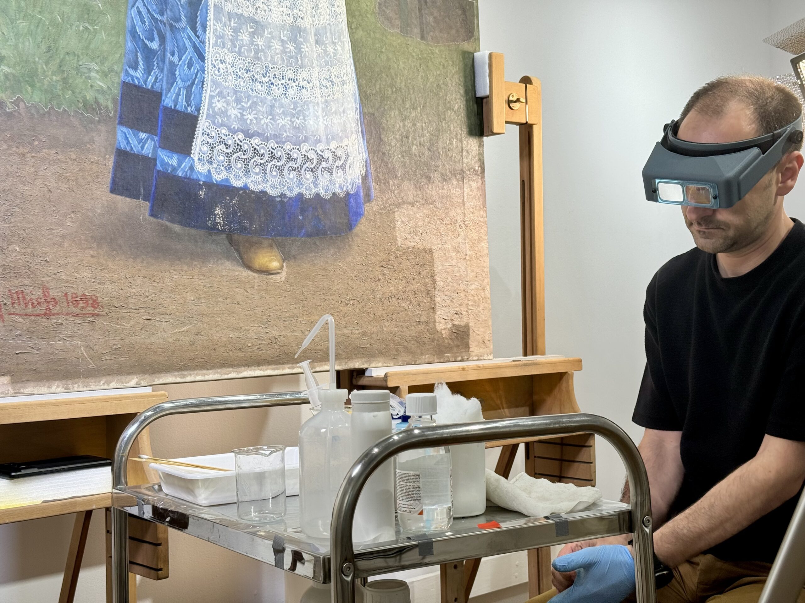 Masa de lucru a restauratorului și zona din tablou în care lipsește culoarea pe pânză (partea de jos a rochiei)